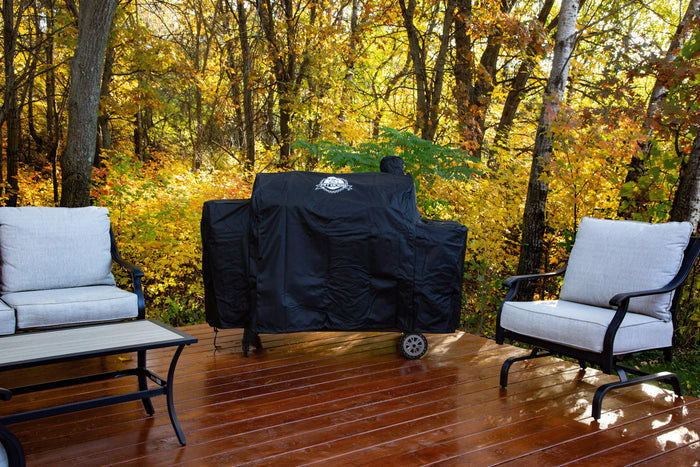 Black Pit Boss Grills 1230 Competition Series Grill Cover on a wooden deck with outdoor furniture and autumn trees in the...