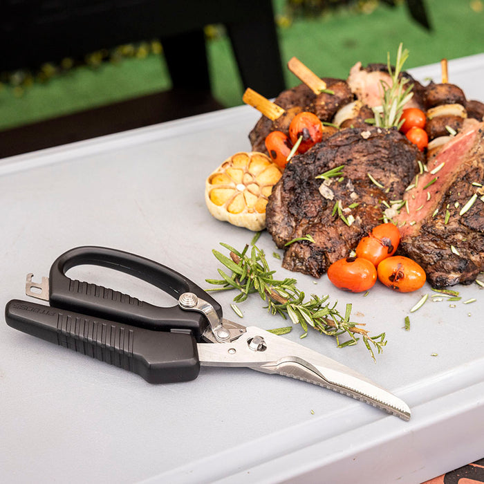 Pit Boss BBQ Shears next to smoked meat and herbs on grey cutting board