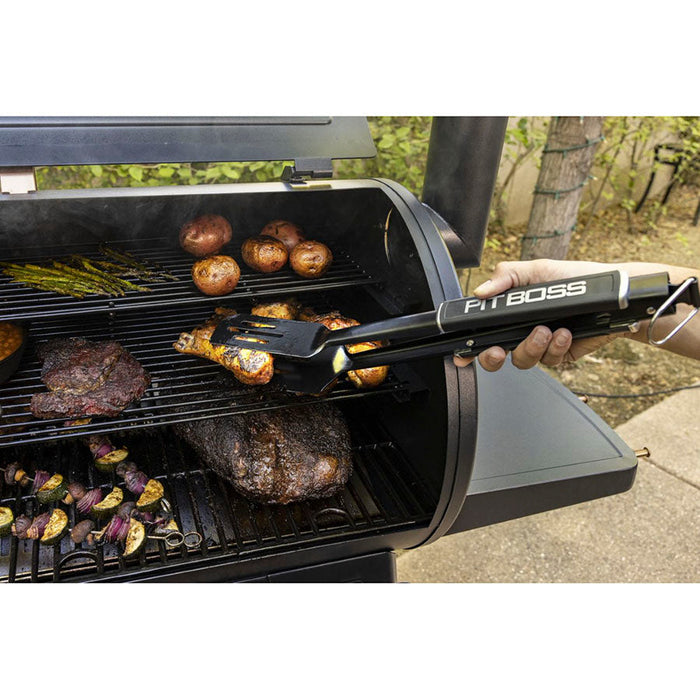 Close up of grilling tools being used on grill with meats and veggies cooking on all three grilling racks. Meats being taken out of grill.
