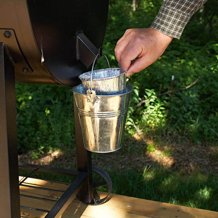 Silver foil liner from Pit Boss Grills being placed in a metal bucket for use with cooking tools.