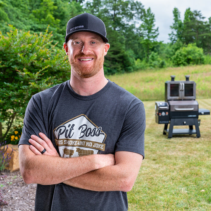 Charcoal heather Pit Boss Grills "Masters of Smoke" men's t-shirt with crossed arms, outdoor setting.