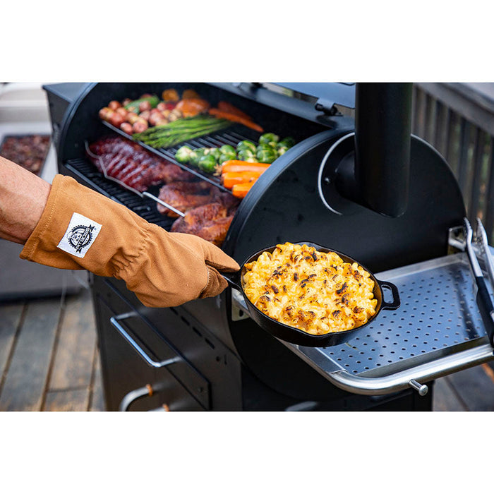 using gloves to handle a cast iron pan of mac and cheese fresh off of the grill