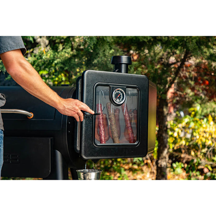Smoker on the side of a grill outside by trees. Sausages hanging smoking.