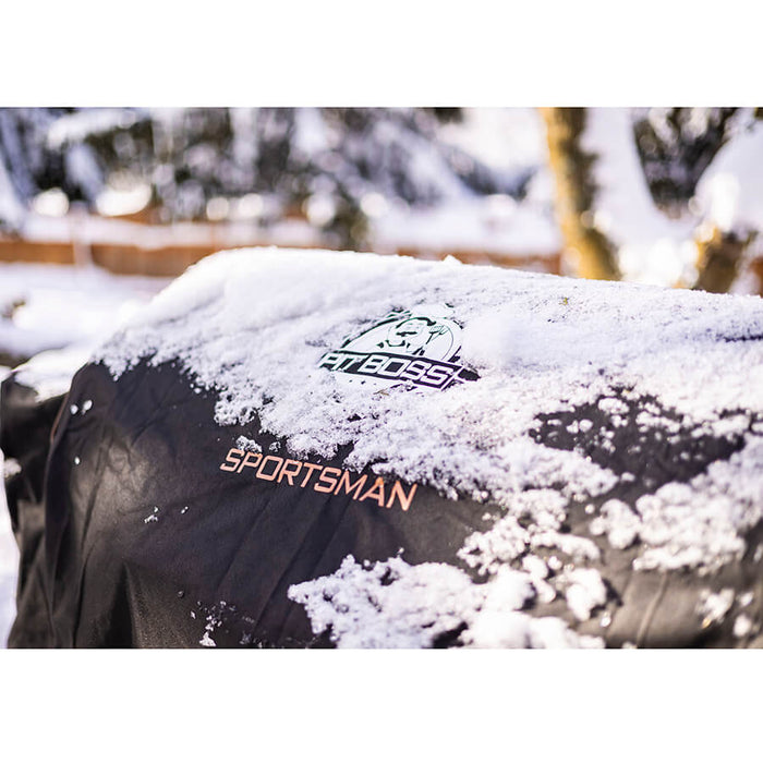 black and orange bbq grill cover outside in snow. detail shot of pit boss grills sportsman logo