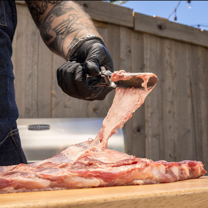 Stainless Steel Rib Prep Tool by Pit Boss Grills, used for precision cutting on a wooden board.