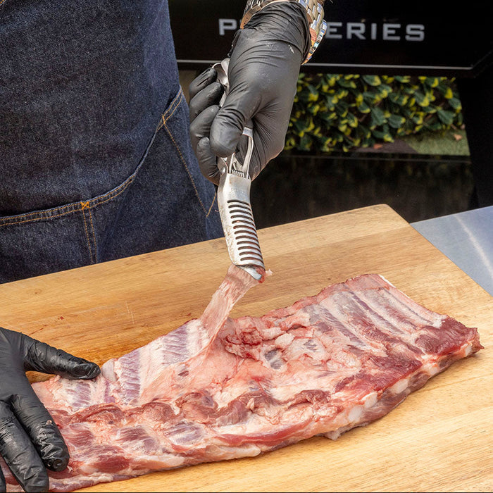 Stainless Steel Rib Prep Tool by Pit Boss Grills, used for trimming ribs on a wooden cutting board.