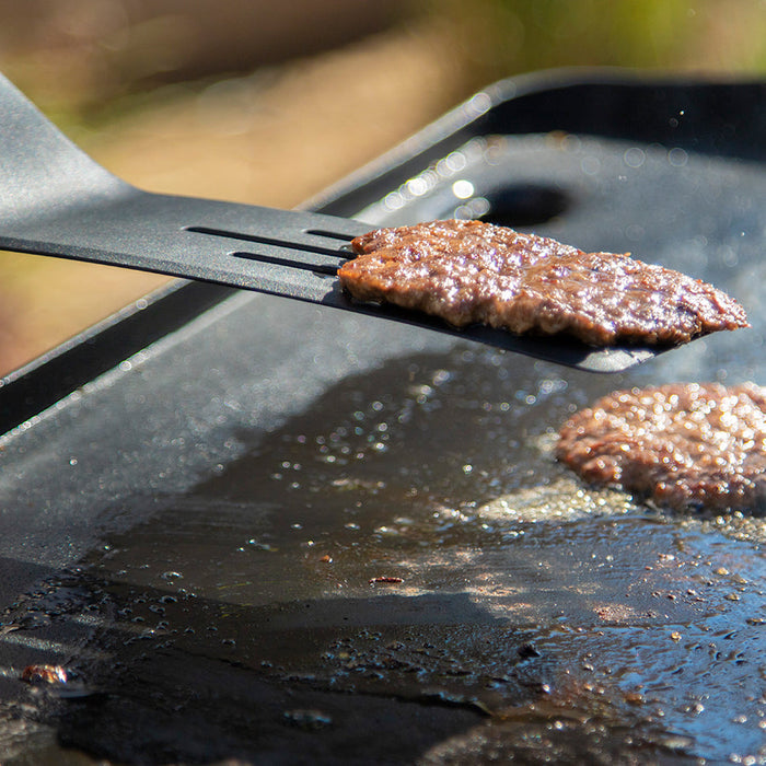 Close up of the black spatula flipping a burger.