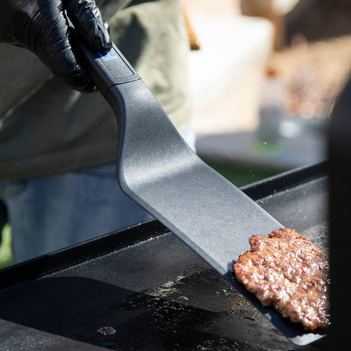 Close up of the black spatula flipping a burger. Side viewpoint.