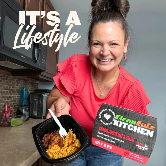 Woman holding a Clean Eatz Kitchen Bourbon Chicken Mac & Cheese grab-and-go meal with 30g protein in her kitchen